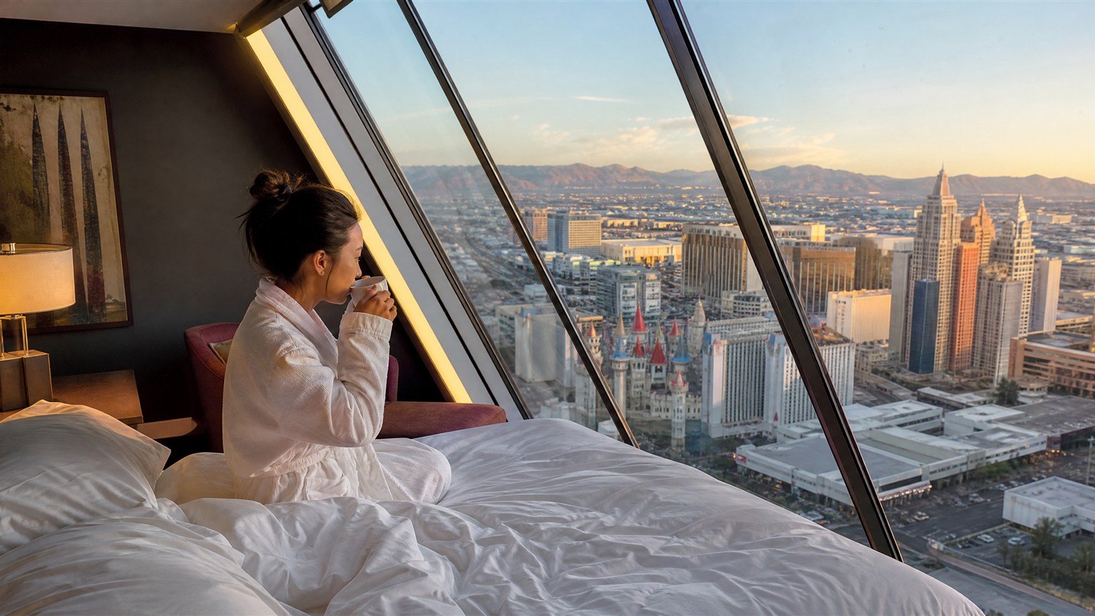 Woman with coffee beside the slanted window of a Luxor Pyramid room overlooking the Las Vegas Strip