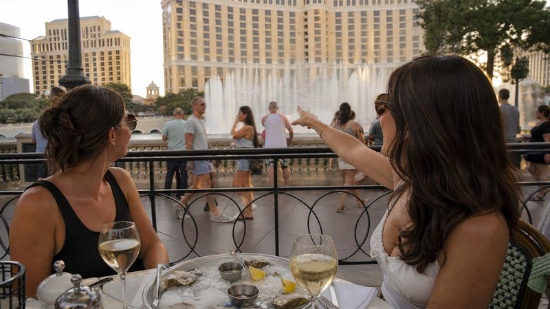 Friends sharing oysters and wine facing the Bellagio Fountains during Las Vegas happy hour deals at Mon Ami Gabi